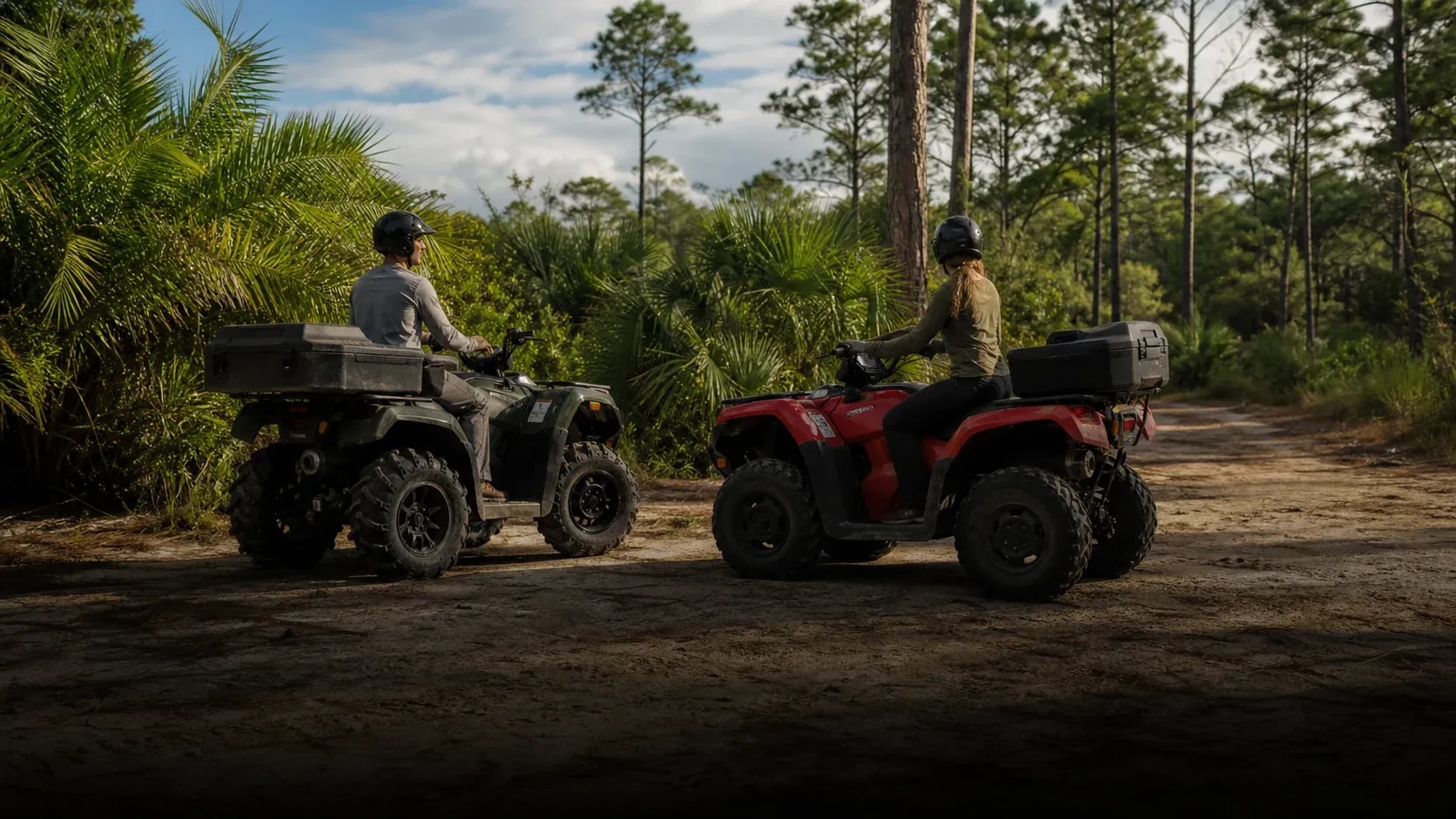 Two helmeted adults stopped on separate all-terrain vehicles